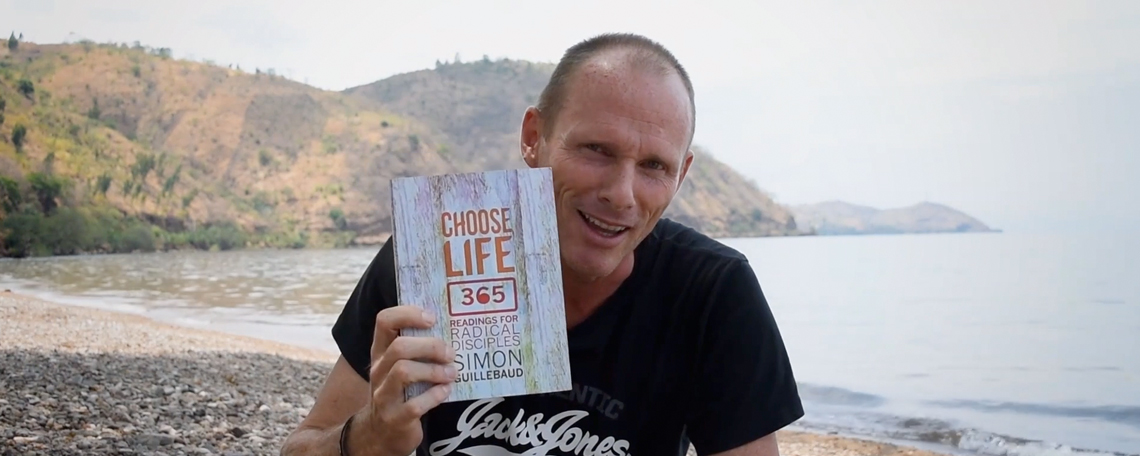 simon holds up the choose life 365 book by a lake