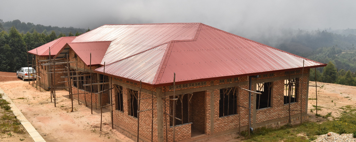 a nearly-completed building with a red roof and with scaffolding atop a hill