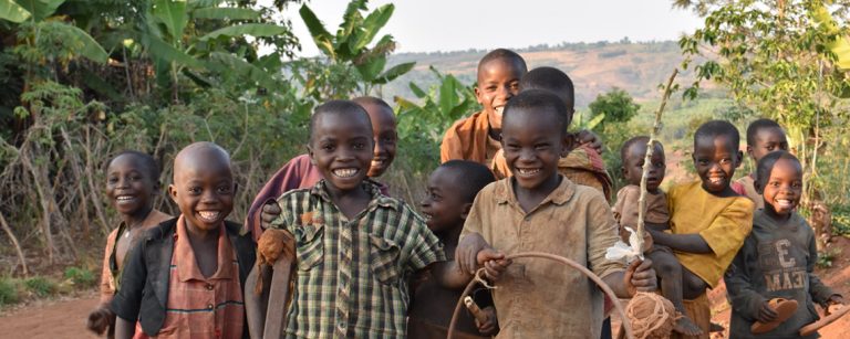 a group of Children pose and smile for the camera in the evening light, one holds a hoop