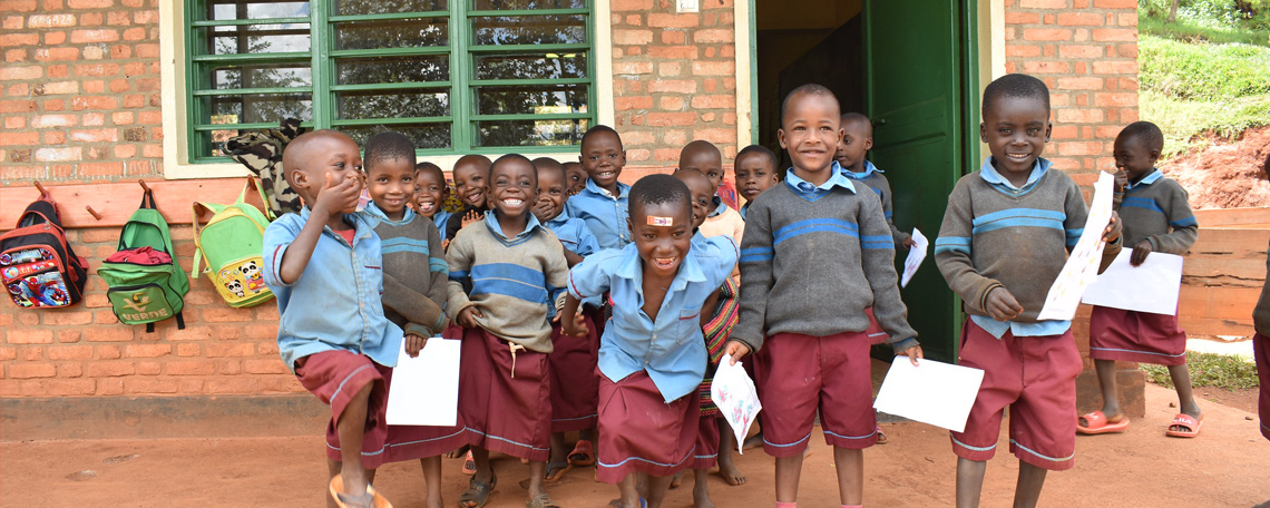 A group of schoolchildren in uniform smile and laugh together outside their classroom