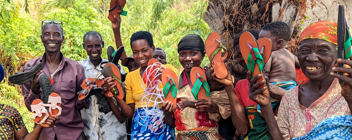 The disabled shoe making group proudly hold up their creations, smiling
