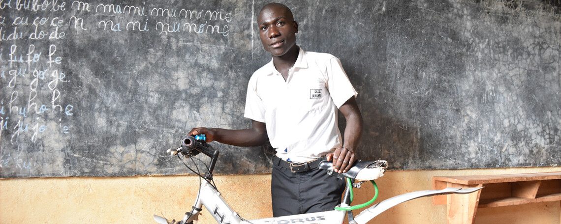 gervais smiles in a classroom with his bicycle