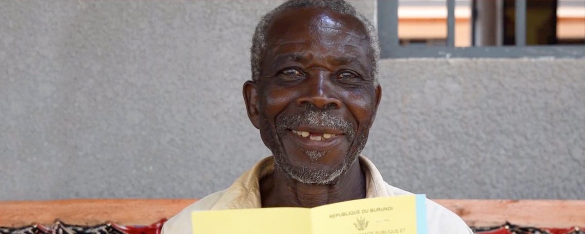 an elderly Burundian man smiles as he holds up his new health card