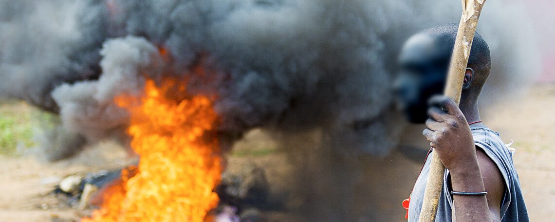 a man with a staff stands next to a fire in the street
