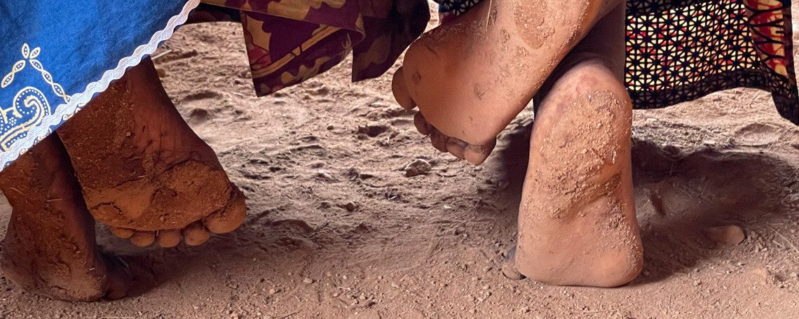two ladies feet underneath a bench upon a dirt floor